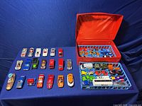Top view of 44 toy cars laid out on a blue surface with two display cases, one red and one white tray.