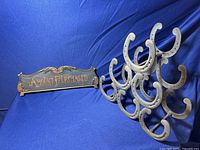 Wide view of antique 'Amount Purchased' brass cash register sign and horseshoe shaped metal wine rack holder on a blue background.