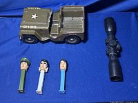 Metal Tonka Army Jeep in olive drab next to black rifle scope and three Elvis-themed PEZ dispensers featuring three different Elvis head designs.