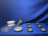 Full lot on blue surface showing seven ashtrays and four small metal decorative items including a vase and shakers.
