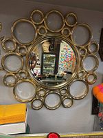 Front view of large round mid-century modern bubble mirror hanging on wall with gold metallic bubble frame and reflective glass center.