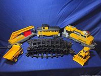 Full set showing battery operated locomotive, caboose, construction vehicles, and black curved tracks on a blue fabric background