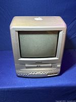 Front view of Apple CRT TV Combo Unit showing screen, control buttons, disc tray, and Apple logo on top.