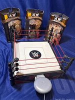 WWE wrestling ring and three unopened AEW action figures displayed on blue background.