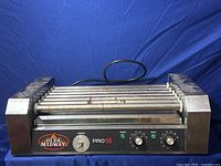 Full view of Olde Midway Pro18 commercial hot dog roller showing all 11 rollers with some rust spots, metallic frame, and power cord.