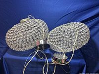 Two crystal orb chandelier lamps with clear crystals in silver metal frames lying on blue fabric background