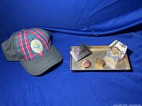 Initial overall photo showing the Cub Scouts cap with multiple collectible items arranged on a metal tray, including pins, badges, a small box, and a paperweight.