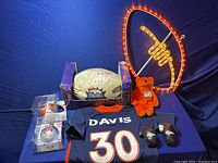 Full lot photo showing signed football, jersey, neon football light, orange plush bear, and mini boxing gloves.