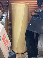 Full view of the fiberglass pedestal showing cylindrical shape, beige color, and some blemishes against window blinds background.