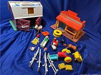 Vintage Fisher Price Play Family Farm barn with various farm animal figures, fences, and accessories, set on a blue background.