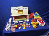 Overview of vintage Fisher Price Family Farm barn, fences, farm animals, farmer figures, and xylophone displayed on blue background.