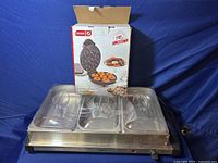 Photo showing the stainless steel three compartment food warmer with transparent lids and the boxed Dash mini donut maker on top.