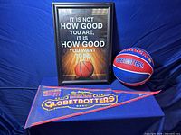 Photo showing framed poster with motivational basketball quote, signed basketball, and Harlem Globetrotters flag on blue cloth.
