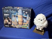 Original box of Harry Potter Hogwarts Great Hall 3D puzzle with 850 pieces, next to plush white owl figurine on wooden stand.