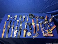 Full lot of 29 watches displayed on blue fabric, showing wide assortment of styles and bands