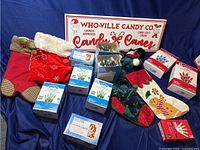 Image displaying three Christmas stockings, one red Christmas-themed bag, multiple boxed Christmas string lights, and a Who-Ville Candy Co sign on blue backdrop.