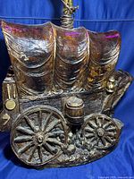 Close-up view of the front and side detail of the painted plaster covered wagon lamp showing wagon wheels, barrel, and lantern details with textured finish.