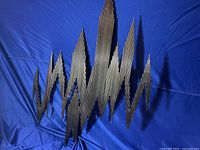 Front view of large MCM metal wall art sculpture made of welding rods with zigzag abstract design laid on a blue backdrop.