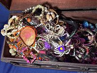 Close-up photo showing mixed colorful beaded jewelry items inside wooden chest, highlighting necklaces, bracelets, and decorative pieces.