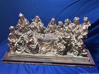 Front angled view of the gold-painted alabaster statue depicting The Last Supper with figures seated at a table on a base labeled 'L'ORIGINE'.