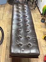 Top view of brown leather/vinyl bench with button tufting, showing padded seat and wear spots.