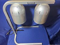 Front view of Nemco dual head heat lamp with two heating heads and metal U-shaped frame on blue background.
