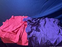 Photo showing pink and purple youth t-shirts piled together on a blue background, showcasing the colors and fabric texture.