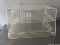 Front and side views of the large clear acrylic pastry display box showing the hinged door and removable trays inside.