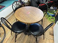 Round wood grain finish table with metal base surrounded by four black metal chairs with padded vinyl seats.
