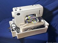 Sewing machine with base, fabric inside, foot pedal and cords organized within the base.