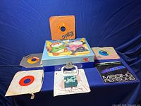 Wide view of Shirt Tales record player box lid featuring cartoon characters, surrounded by six 45 RPM vinyl records with diverse sleeve designs.