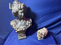 Photo of woman bust statue and decorative skull on blue background