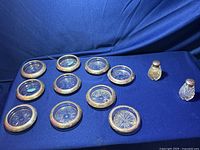 Overall view of 9 sterling silver rimmed crystal coasters and 2 sterling and crystal salt and pepper shakers on blue fabric background.