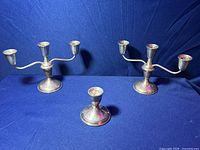 Three sterling silver weighted candle holders: two large three-arm holders and one smaller single holder, set on a blue cloth background.