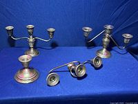 Four Lapier sterling silver weighted candle holders arranged side by side on a blue background. Two candelabras with two candle sockets each and two single candlesticks with round weighted bases.