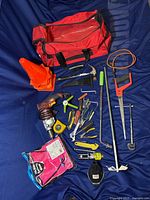 Full display of tool lot including red tool bag, hand tools, power tools, safety cones, and other items spread out on blue fabric background.