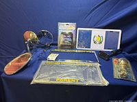 Photo showing vintage chrome mirrors, multiple packaged Colorado Christian University license plate frames, a white license plate holder with blue emblem, a small black mounting bracket, and a packaged chrome trailer ball.