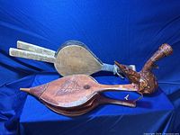 Photo showing two wooden fireplace air blowers and ornate carved leather bottle with strap on blue background.