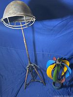 Full view of both items showing the WWII metal helmet floor lamp on tripod stand alongside the colorful hot air balloon windchime.