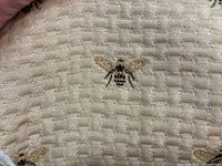 Close-up of beige textured basketweave fabric with embroidered bee motif