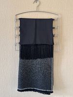 Cashmere shawl hung on metal rack showing black top panel, fringe detail and grey gradient bottom