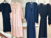 All four dresses hung side by side—black viscose, pink silk, navy silk two-piece, black silk embellished