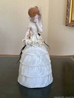 Porcelain pin cushion doll figurine with a netted veil and fabric dress details, standing upright on a table.