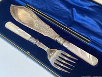 Fish serving set in an open blue velvet-lined case showing the knife and fork; knife blade engraved with floral design, mother-of-pearl handles polished and lustrous.