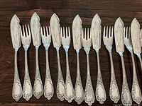 Close-up of six fish serving knives and six forks showing fish engraving and bubble detail.