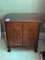 Front view of antique style walnut media cabinet with decorative carving on doors and base, showing overall condition.