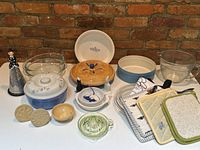 Front view of assorted bakeware including novelty grater, mixing bowls, covered casserole, cookie stamps, citrus juicer, ramekin, blueberry pie dish, baking dishes, then pot holders and measuring cup