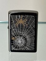 Front view of black chrome Zippo lighter with gold spider and silver web design.