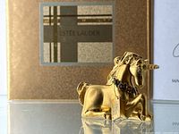 Gold-tone Estée Lauder unicorn figurine with floral garland and original tag attached, viewed side angle showing detailed horn and mane.