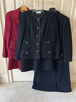 Three tweed garments on hangers against door: red set, black set, long black jacket